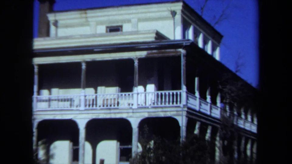Closer 1971 Maine 8mm view of the large house facade, showing white railings, porch columns, arched lower openings, chimney, and surrounding trees.