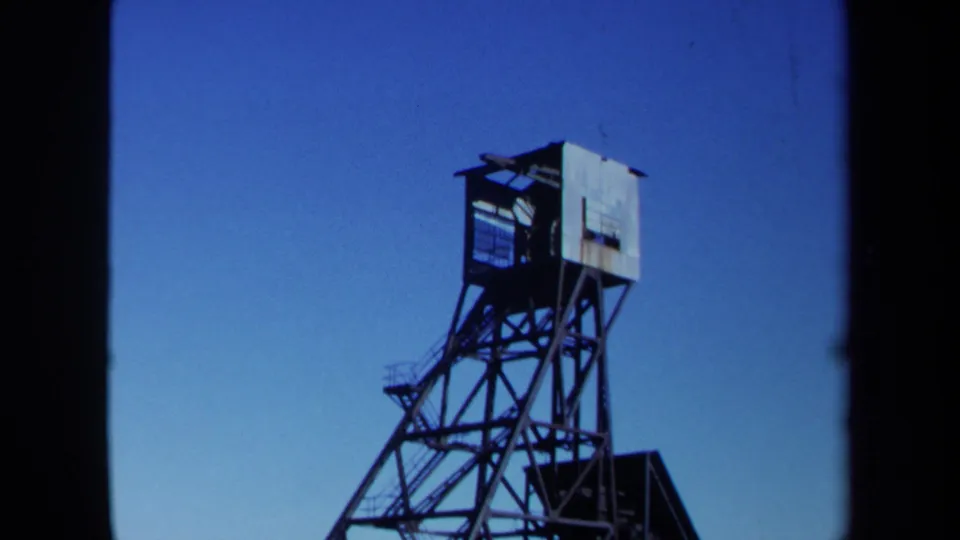 1971 Maine home-movie frame of a metal industrial tower, seen from below with angular supports and a small boxlike structure at the top.