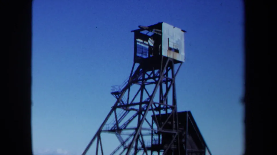 1971 Maine 8mm frame showing the upper portion of a steel mine derrick or headframe against blue sky.