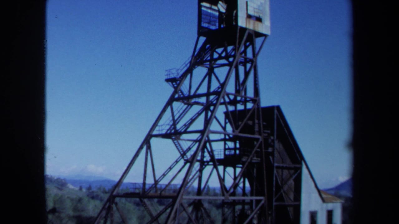 1971 Maine 8mm frame showing a tall industrial derrick with forested hills and distant mountains behind it.