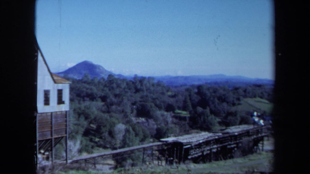 Distant mountain above trees with a wooden trestle and part of a white building at left.