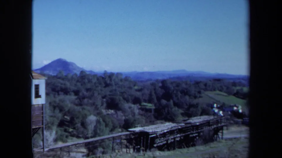 1971 Maine 8mm view across trees and a wooden trestle toward a distant hill under a clear blue sky.
