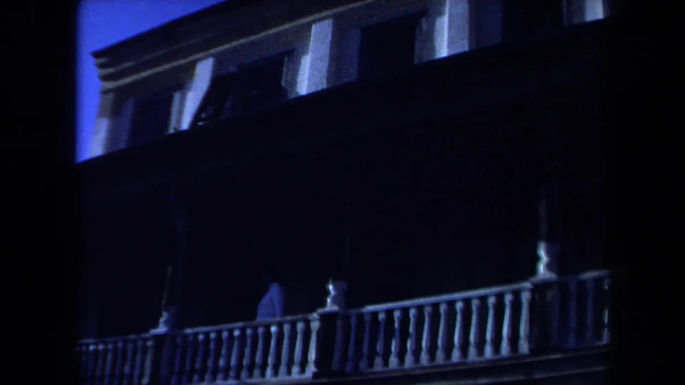 1971 Maine 8mm frame of a large white house exterior, porch railing, columns, upper windows, and deep shadow.