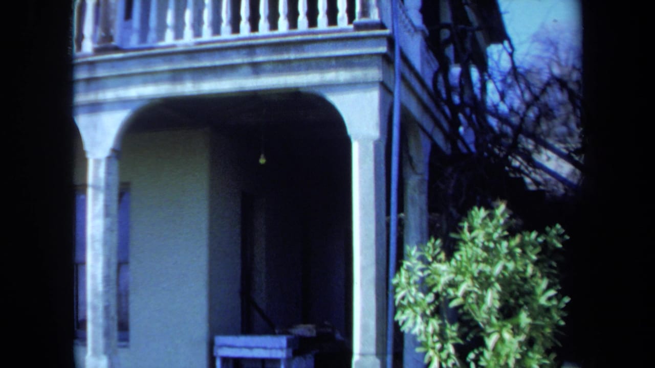 1971 Maine 8mm frame with arched lower porch openings, white railing, shrubbery, and a shadowed entry beneath the veranda.