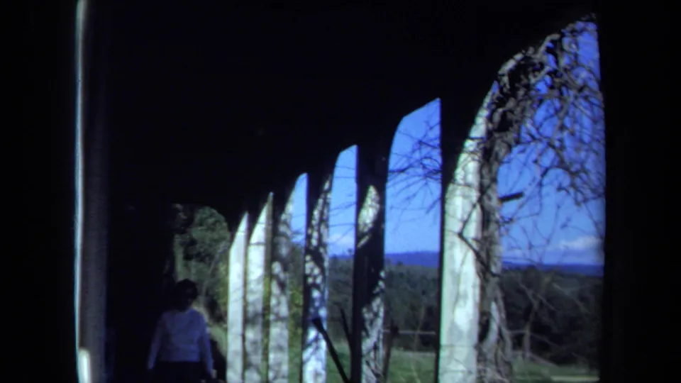 1971 Maine 8mm frame showing a person inside a dark abandoned structure with arched openings and blue sky outside.