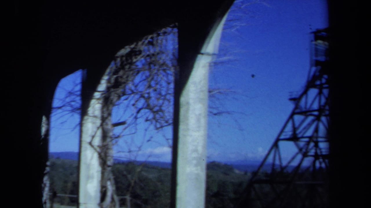 Arched openings frame bare branches, blue sky, and a distant tower.