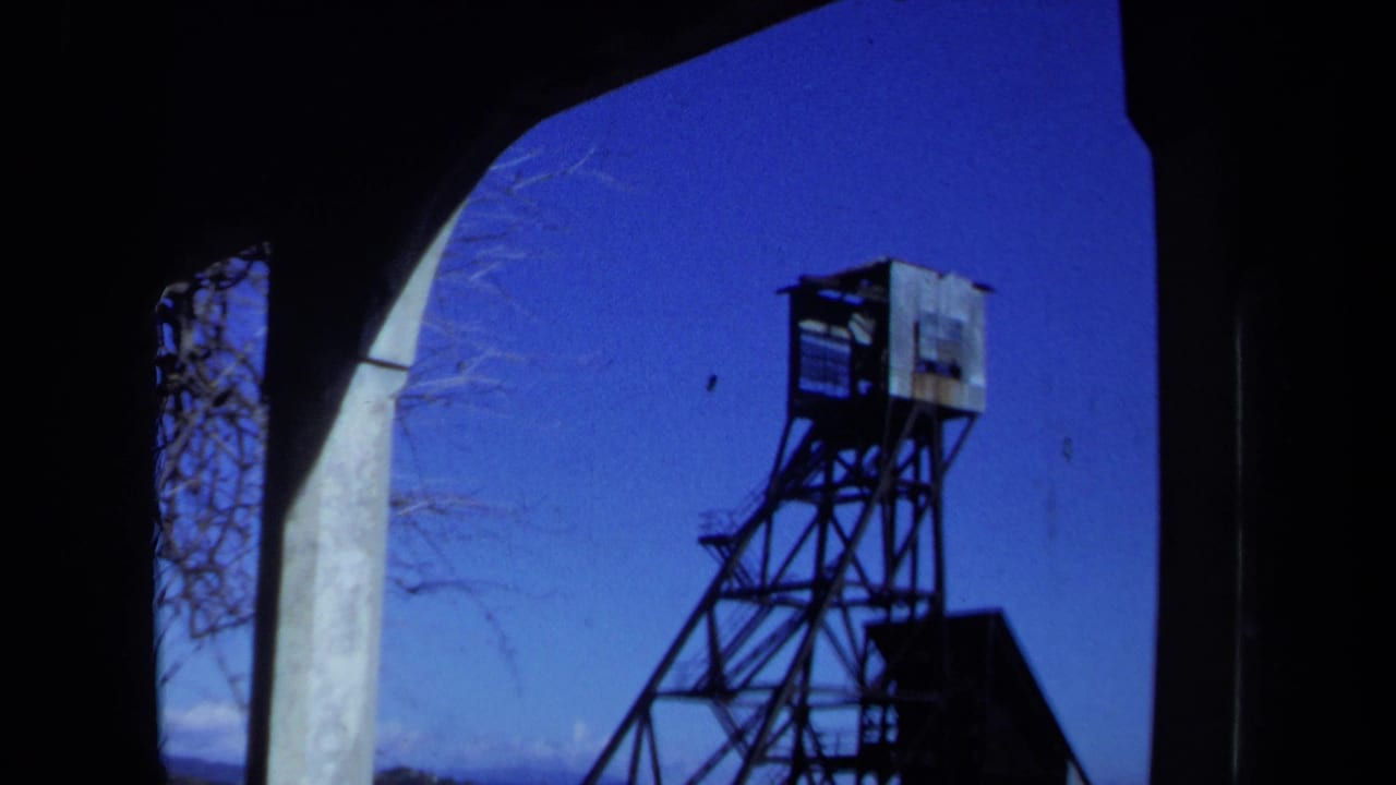 1971 Maine 8mm frame of a weathered tower outside an abandoned arched structure under a clear blue sky.