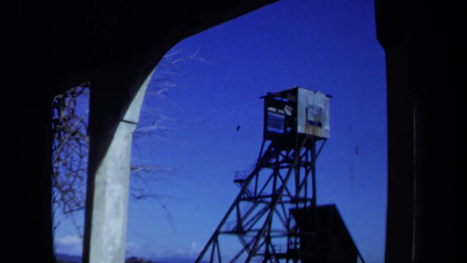 1971 Maine 8mm frame of a weathered tower outside an abandoned arched structure under a clear blue sky.