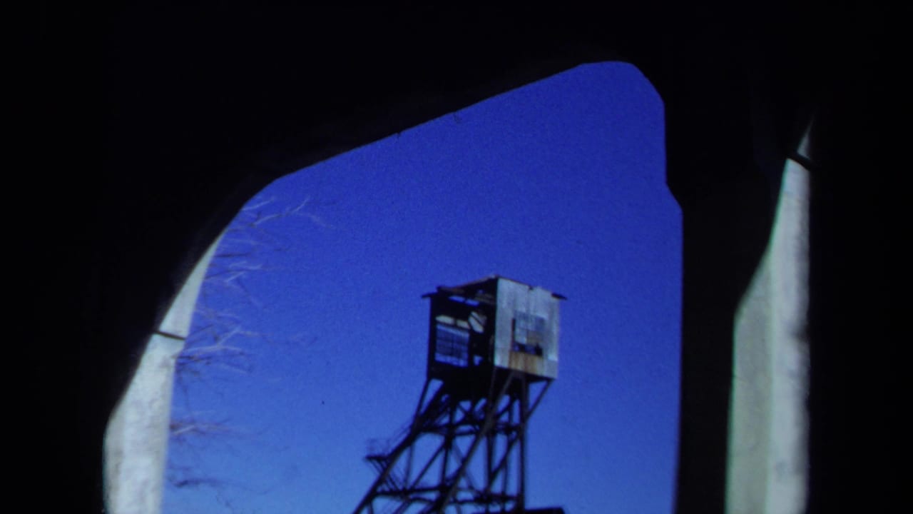Final 1971 Maine frame holding on a weathered tower viewed through the shadowed arch of an abandoned building.