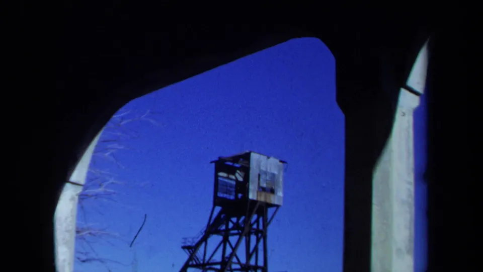 1971 Maine 8mm frame showing a weathered mine headframe viewed through a dark arched foreground under a deep blue sky.