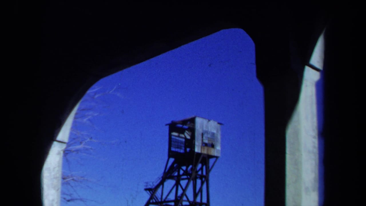 Distant mine headframe framed by dark foreground edges and blue sky.