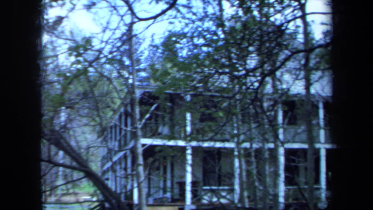 Final 1971 Maine frame shows the side of the two-story house and porch structure through trees, with cool color shift and soft focus.