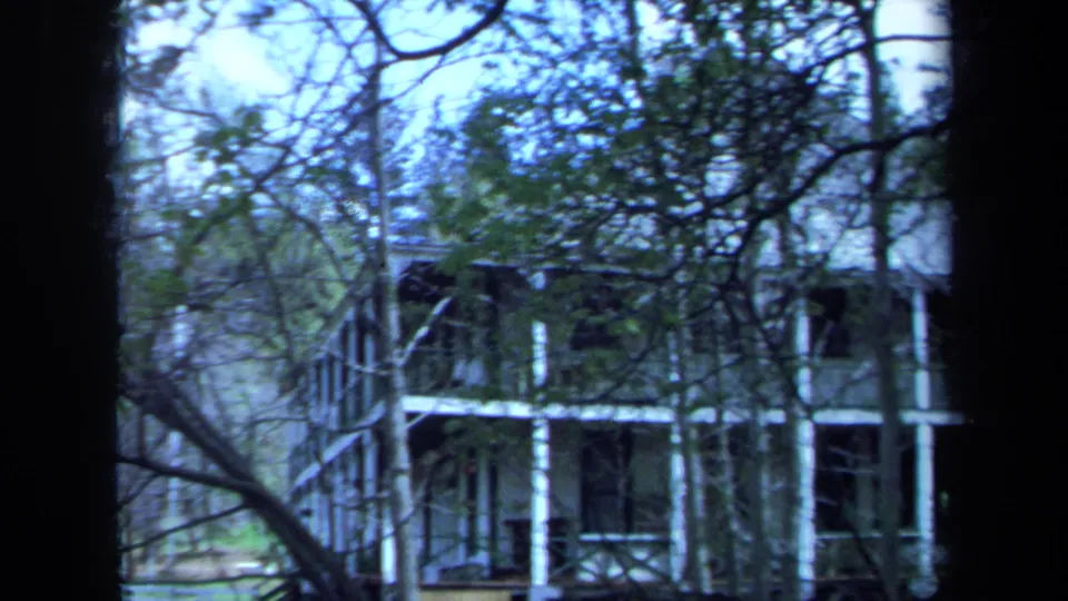Final 1971 Maine frame shows the side of the two-story house and porch structure through trees, with cool color shift and soft focus.