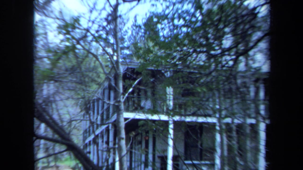 Two-story white house partly obscured by trees and dark film-frame edges.