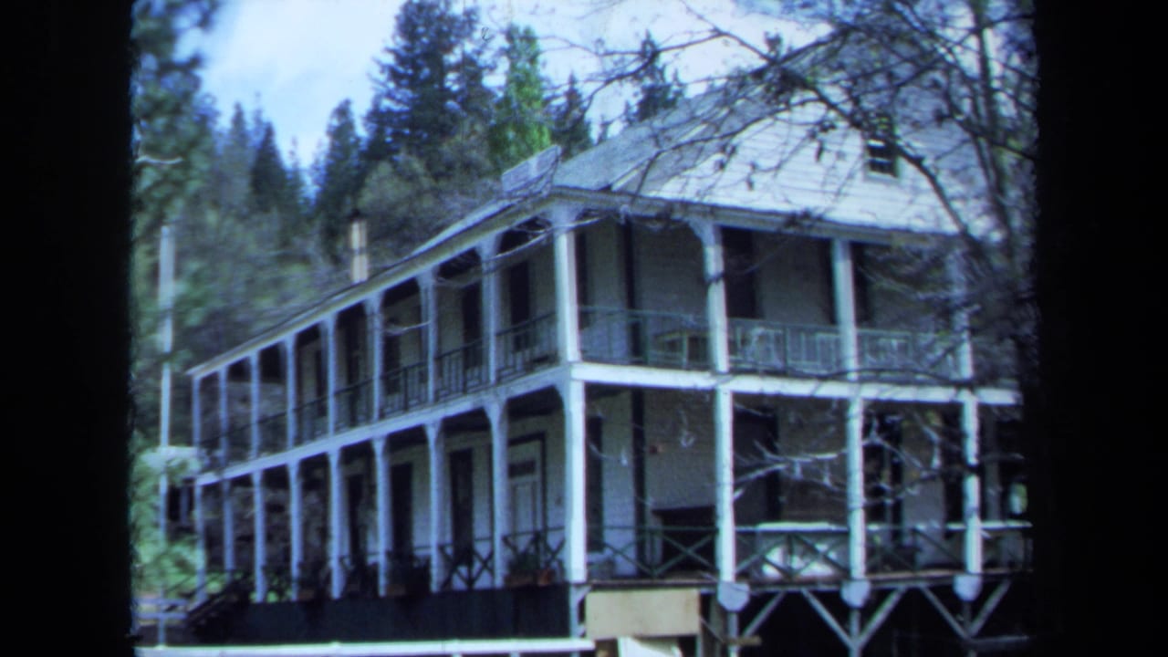 1971 Maine frame showing the side and front of a white two-story house with porches, railings, columns, and surrounding trees.