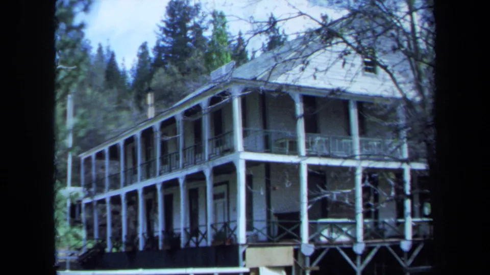 1971 Maine frame showing the side and front of a white two-story house with porches, railings, columns, and surrounding trees.