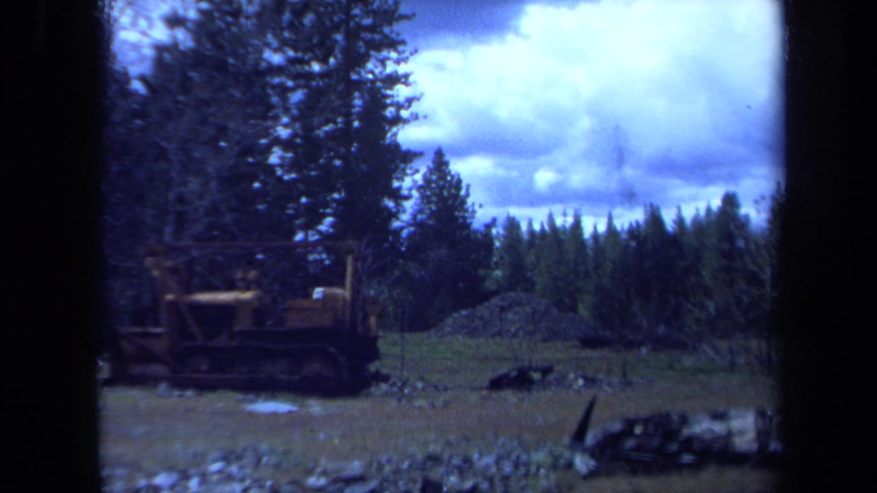 1971 Maine footage frames a yellow bulldozer parked in a rough clearing with evergreen trees and gravel behind it.