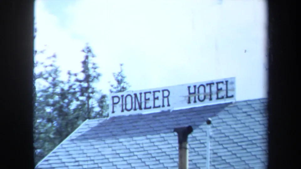 1971 Maine home-movie frame showing the Pioneer Hotel sign above a shingled roof, with a chimney pipe and trees visible.