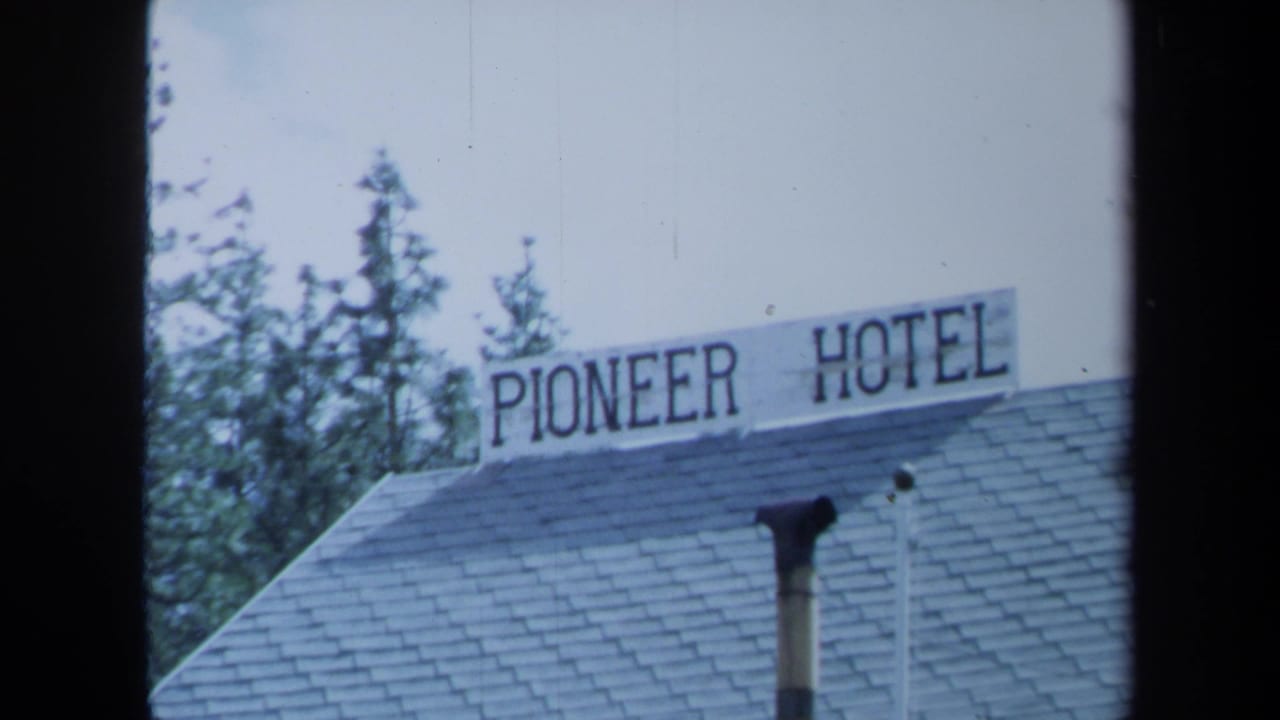 1971 Maine 8mm frame showing a close view of the Pioneer Hotel roof sign, shingled roof, chimney pipe, and pine trees.