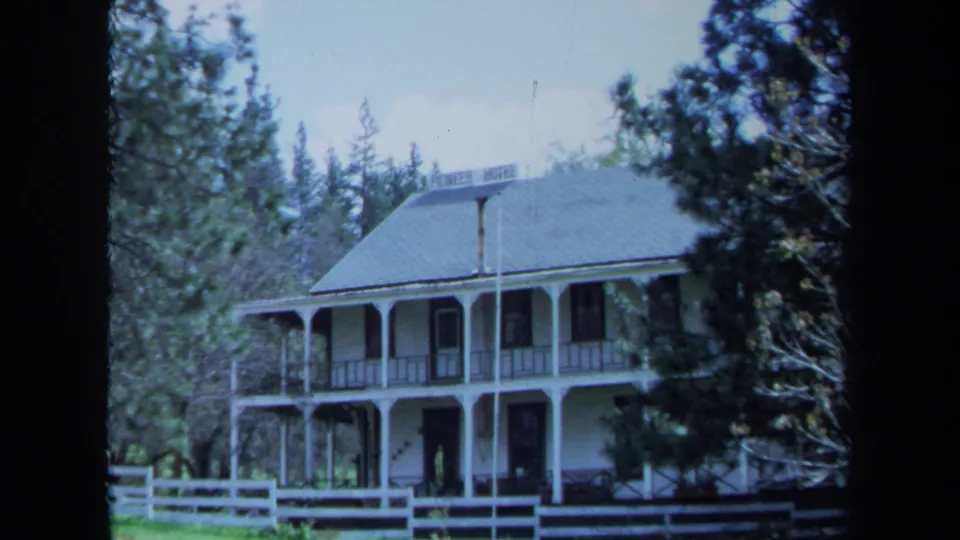 1971 Maine home-movie frame showing the Pioneer Hotel exterior, roof sign, porch, fence, and trees in a wider composition.