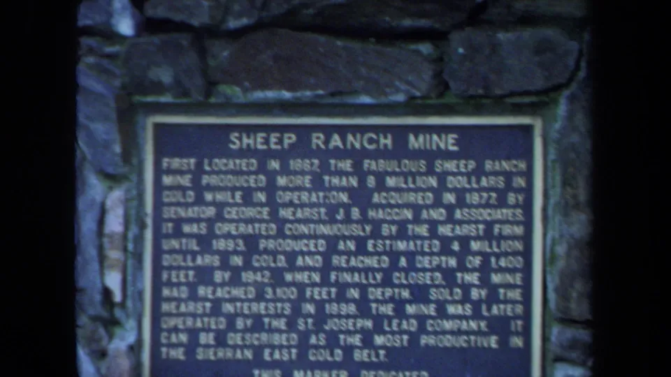 1971 8mm close-up of a Sheep Ranch Mine historical plaque set into a rough stone pillar, with soft focus and dark frame edges.