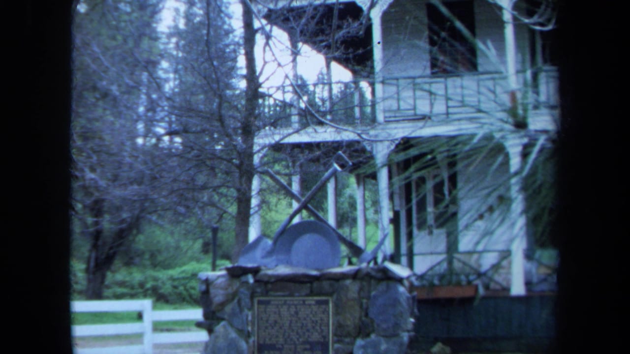 Farmhouse and stone marker seen through dark vertical film frame edges.