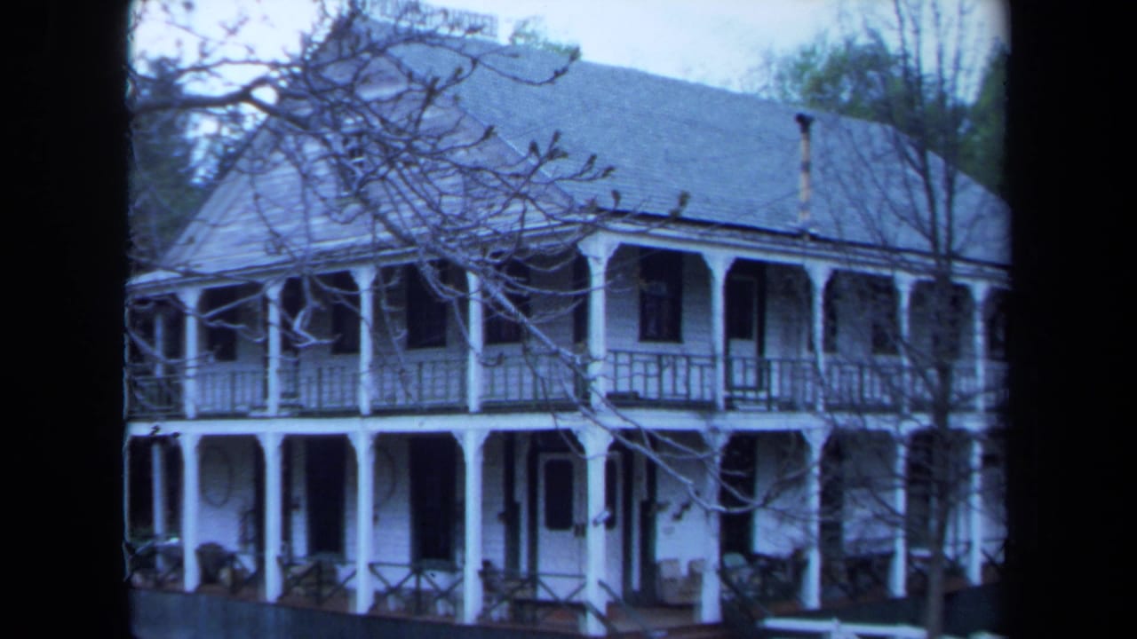 White two-story house with wraparound porch partly obscured by bare branches.