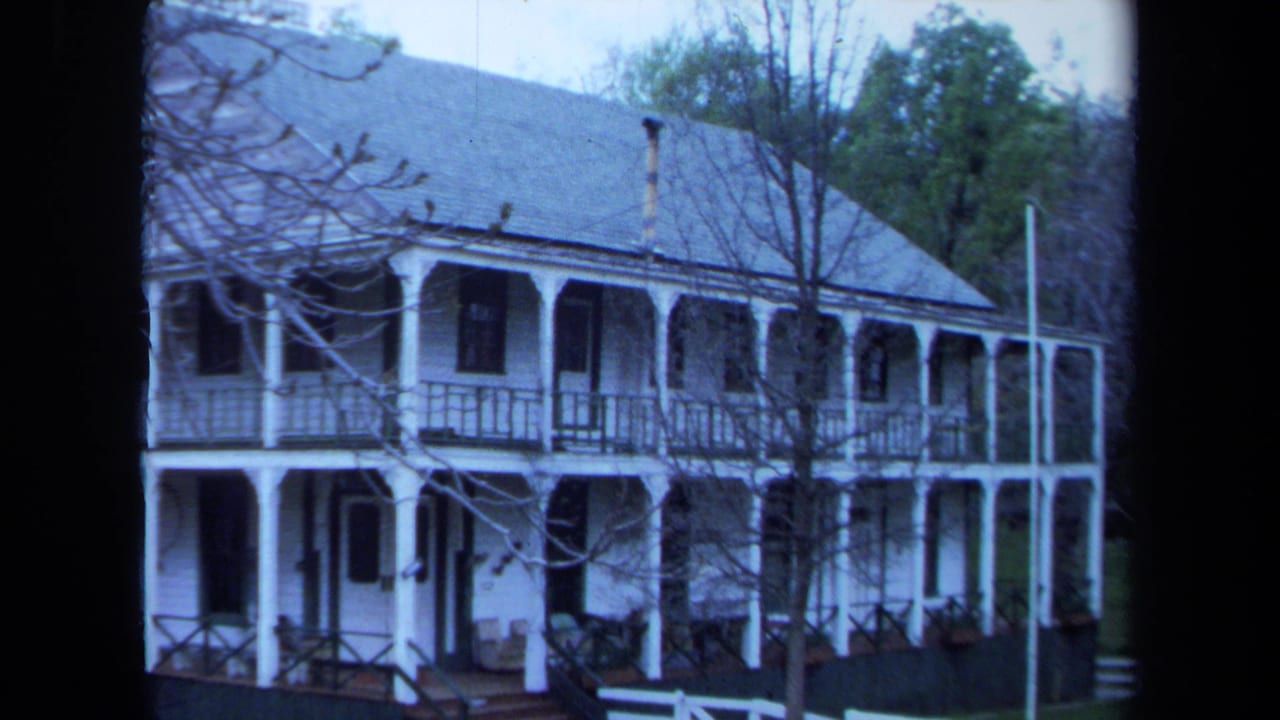 White house facade with upper and lower porches and trees in the background.