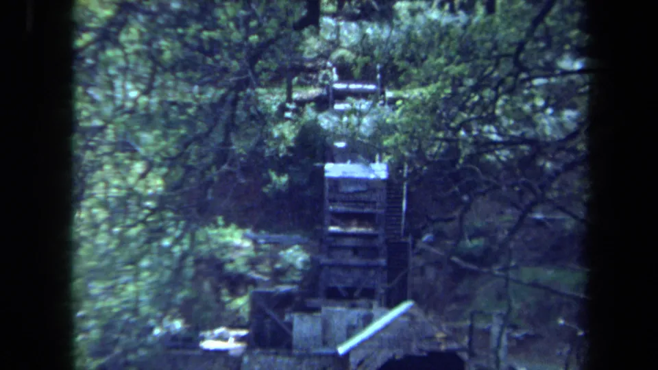 1971 Maine 8mm frame showing a waterwheel and surrounding trees with soft focus and visible film gate edges.
