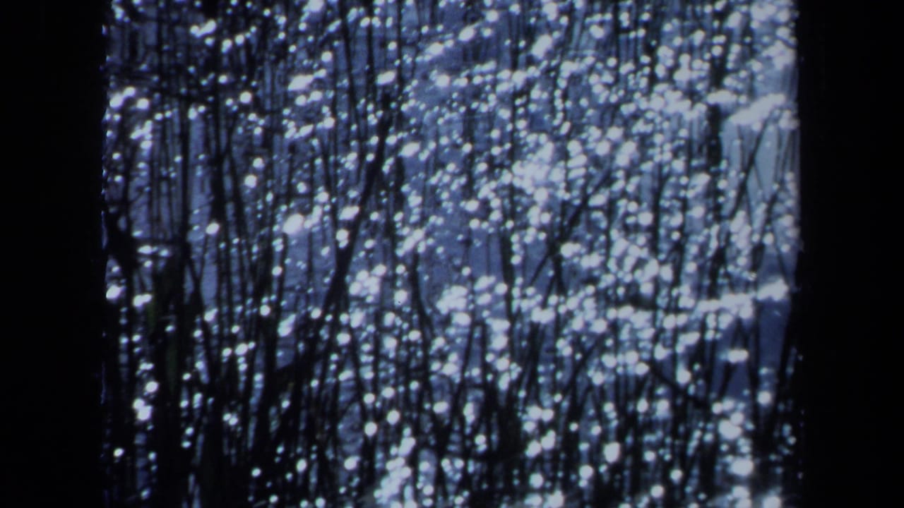 1971 Maine 8mm frame showing a blue, grainy field of bright speckles crossed by dark vertical lines and a central black band.