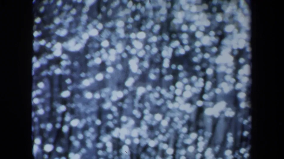 1971 Maine 8mm frame with out-of-focus white dots, dark line patterns, and a blue low-light home-movie texture.