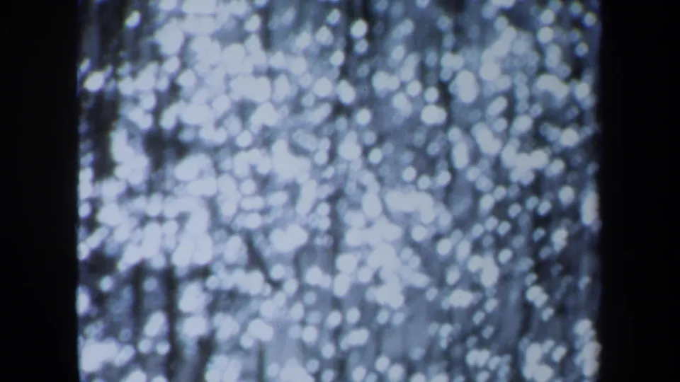 1971 Maine 8mm frame with soft white bokeh, dark vertical divisions, and faint hanging lines against a cool-toned background.