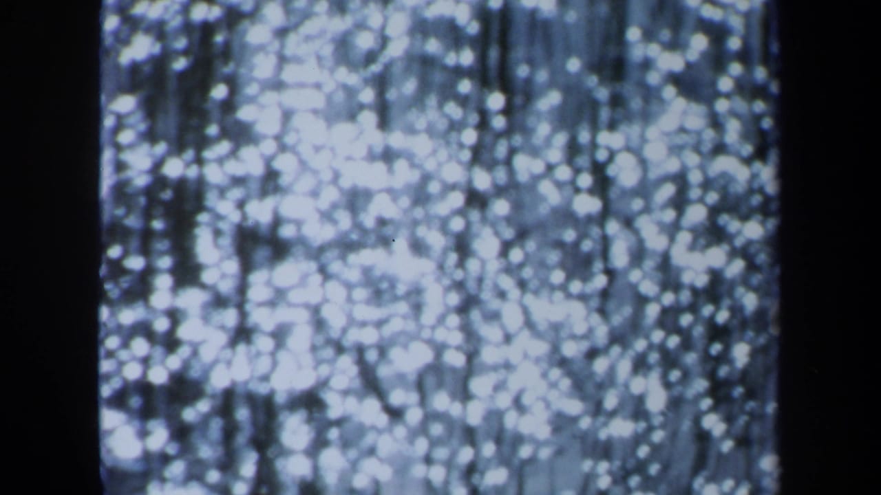 1971 Maine 8mm frame showing bright out-of-focus white lights, thin vertical strands, and a heavy dark band near the center.