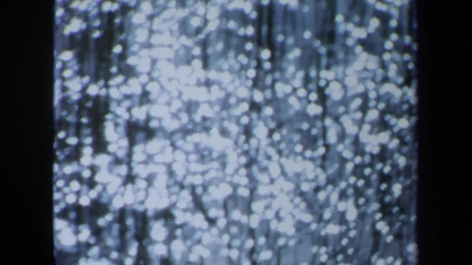 1971 Maine 8mm frame showing bright out-of-focus white lights, thin vertical strands, and a heavy dark band near the center.