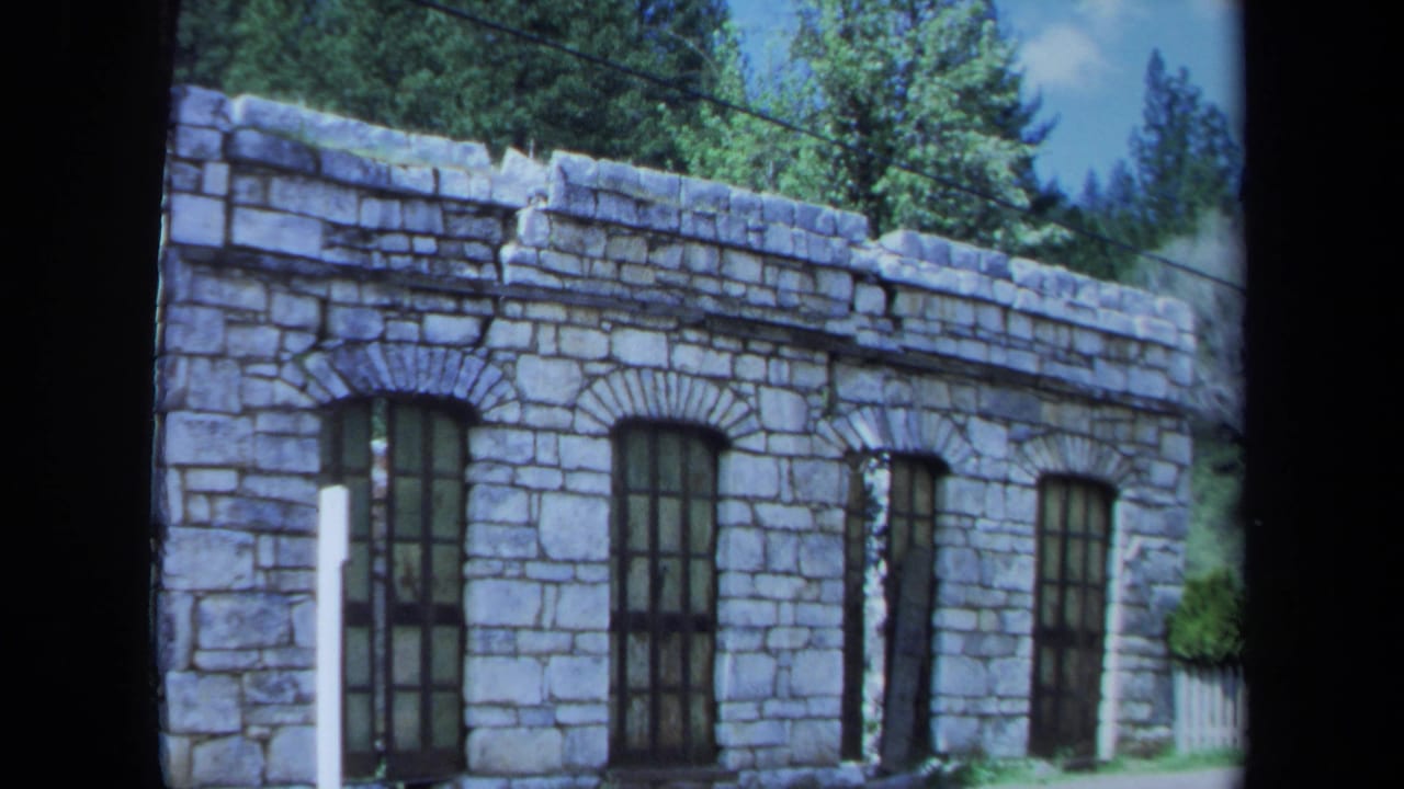 Weathered stone building with arched windows and trees behind it.