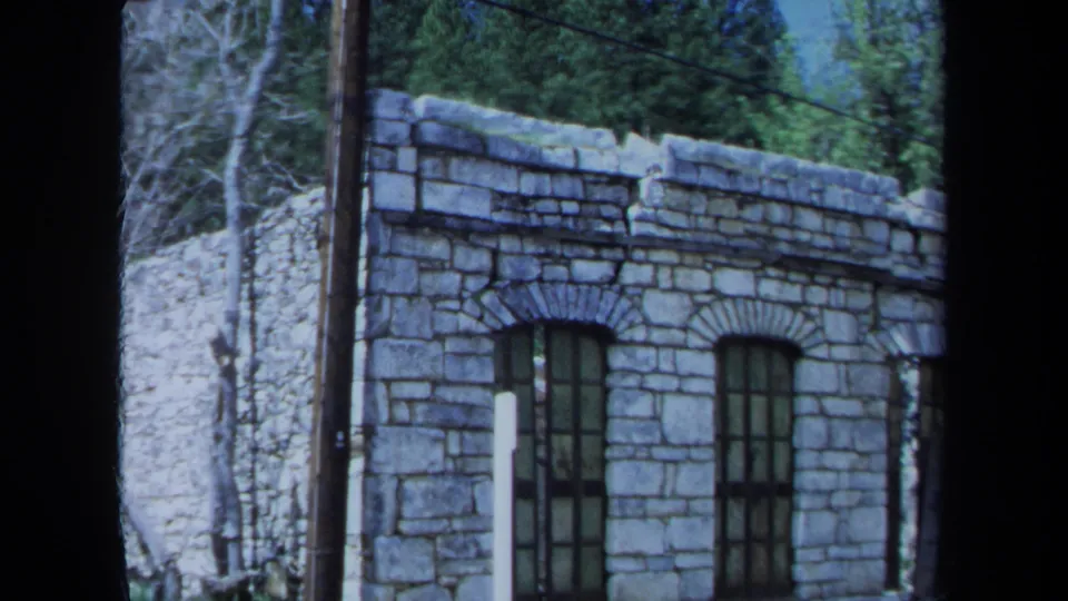 A stone building with arched windows, a utility pole, and evergreen trees appears in 1971 Maine 8mm home-movie footage.