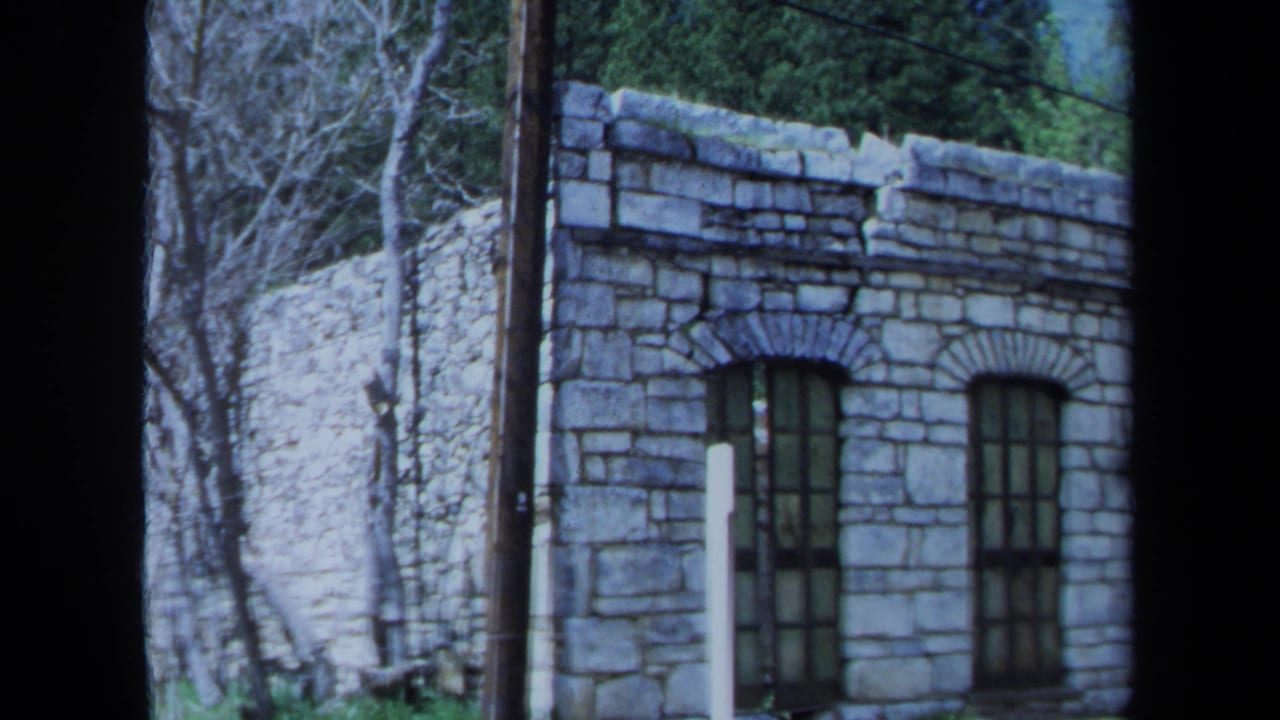 1971 Maine 8mm frame showing a derelict stone facade with arched barred windows, bare trees, and dark film borders.
