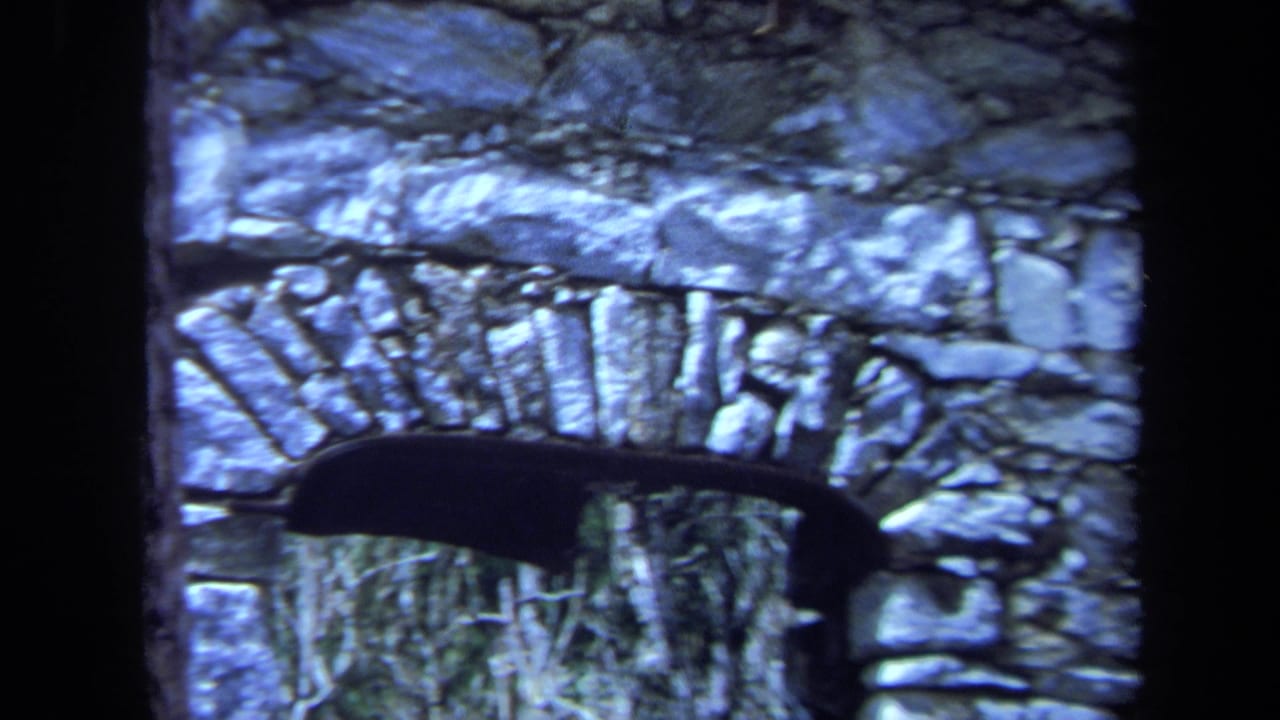 1971 Maine 8mm frame showing a close view of weathered stone arches, dark borders, and vegetation visible through an opening.