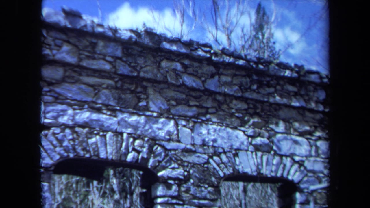 Weathered stone wall with two arched openings beneath a blue sky and bare branches.