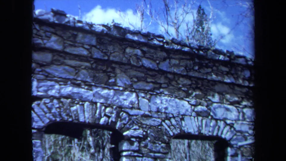 1971 Maine 8mm frame with a wider view of the weathered stone structure, arched openings, sky, and surrounding vegetation.