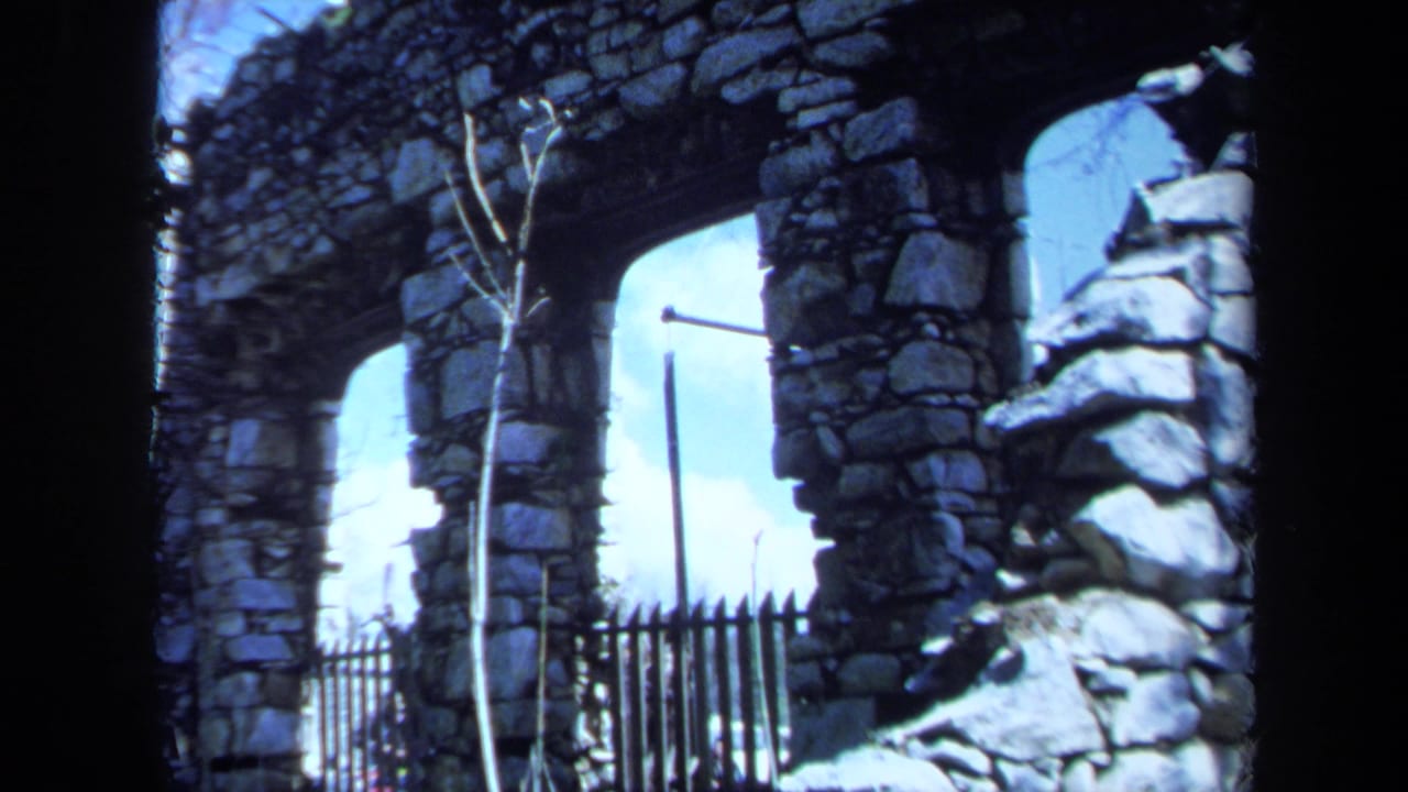 1971 Maine 8mm frame showing a weathered stone archway, rough masonry, bare branches, and a black metal fence.