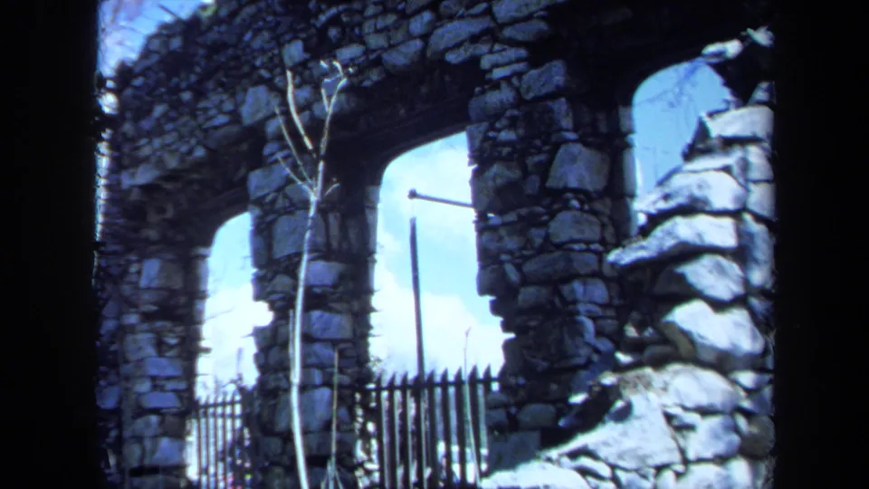 1971 Maine 8mm frame showing a weathered stone archway, rough masonry, bare branches, and a black metal fence.