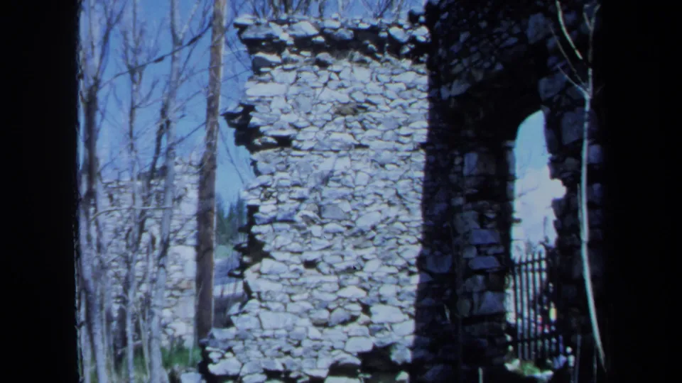1971 Maine 8mm frame of weathered stone masonry, an arched opening, black fence, and winter-bare trees.