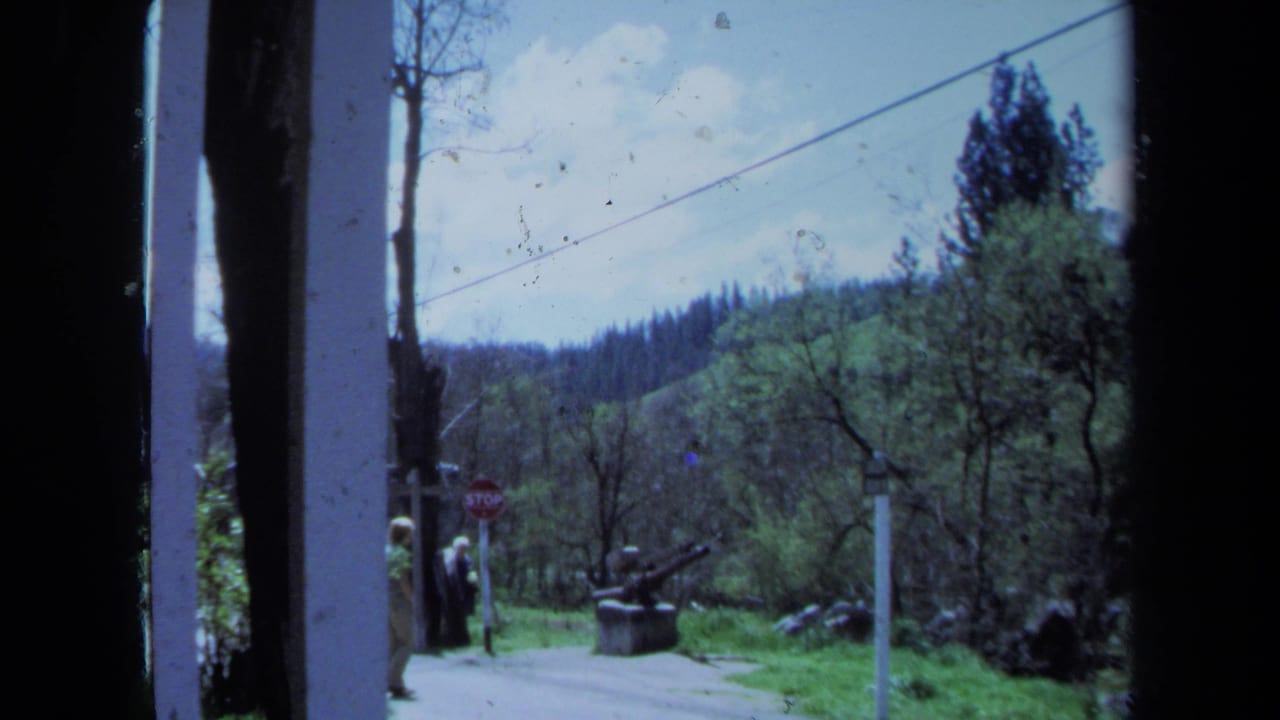1971 Maine home-movie frame showing a rural roadside, wooded hills, overhead cable, stop sign, and two distant walkers.