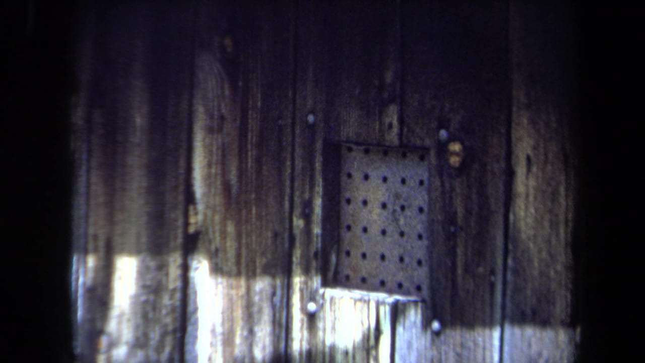 1971 Maine 8mm frame showing a close view of weathered wood and a perforated metal panel at an abandoned military site.