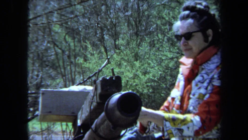 A closer 8mm frame shows the woman in sunglasses beside the cannon barrel, with the forested setting filling the background.