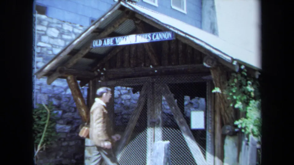 A man approaches the rustic shelter marked Old Abe Volcano Cannon beside a stone building wall in Maine 1971 footage.