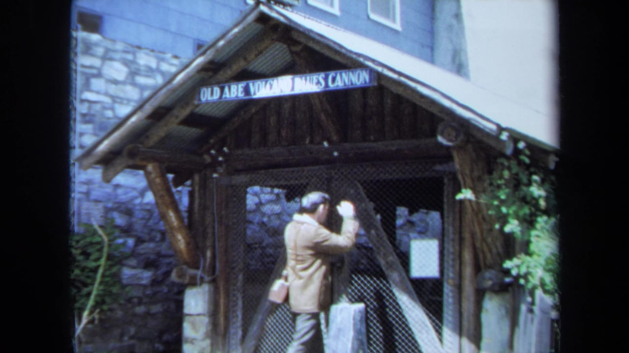 In 1971 Maine footage, a man in a light jacket looks toward a chain-link gate beneath the Old Abe Volcano James Cannon sign.
