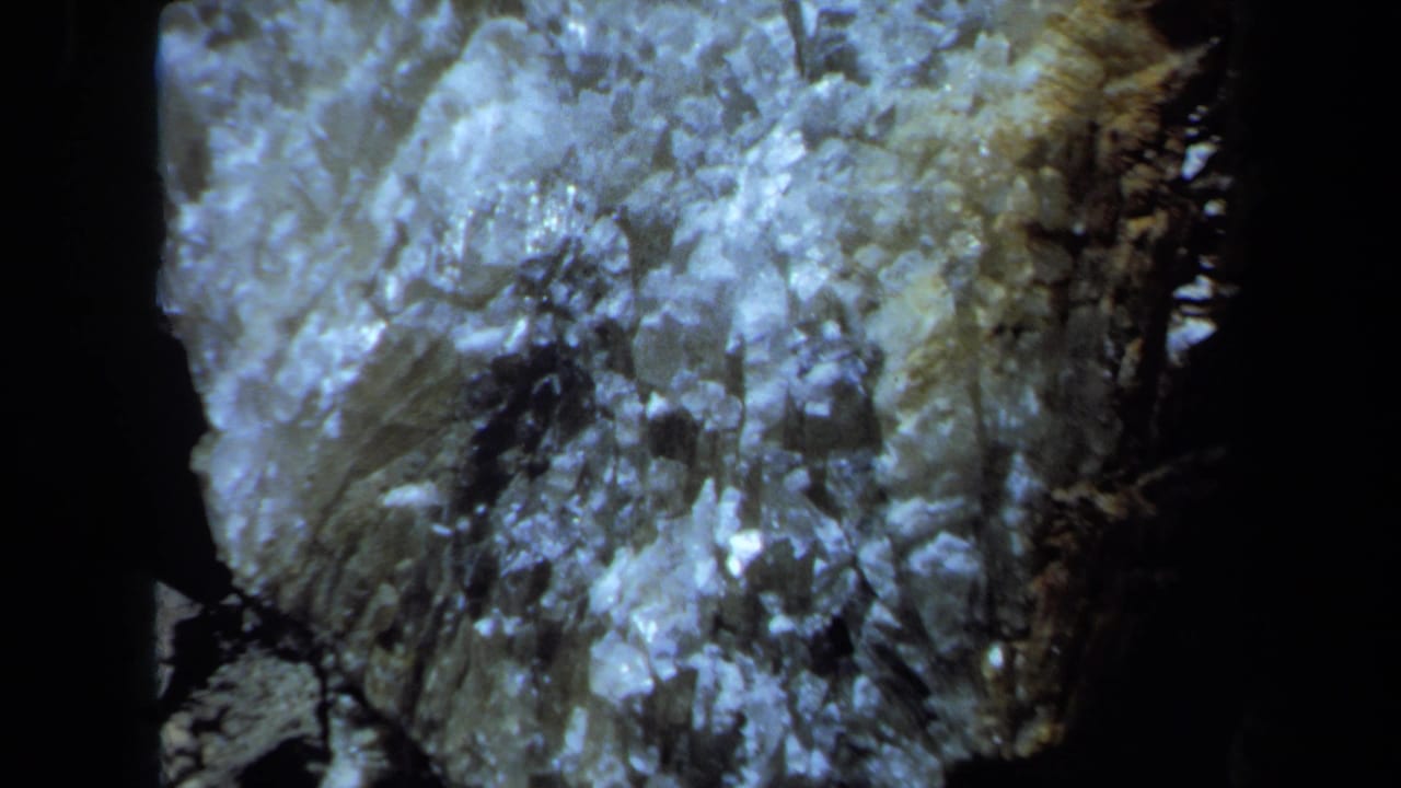 1971 Maine 8mm frame showing a bluish illuminated crystalline rock surface in a dark enclosed setting.