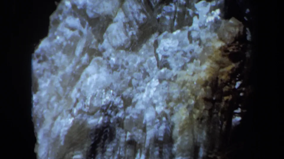 Close 8mm view of a rough crystalline surface in Maine, lit unevenly against a dark void.